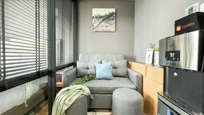 Ett modernt vardagsrum med en grå soffa, en blå kudde, en liten växt och ett självrengörande kylskåp.