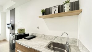 A modern kitchen with a marble countertop, a stainless steel sink, a built-in oven, and a wall-mounted TV. - Studio Apartment Collins Boulevard Near Summarecon Mall Serpong (Gading Serpong)