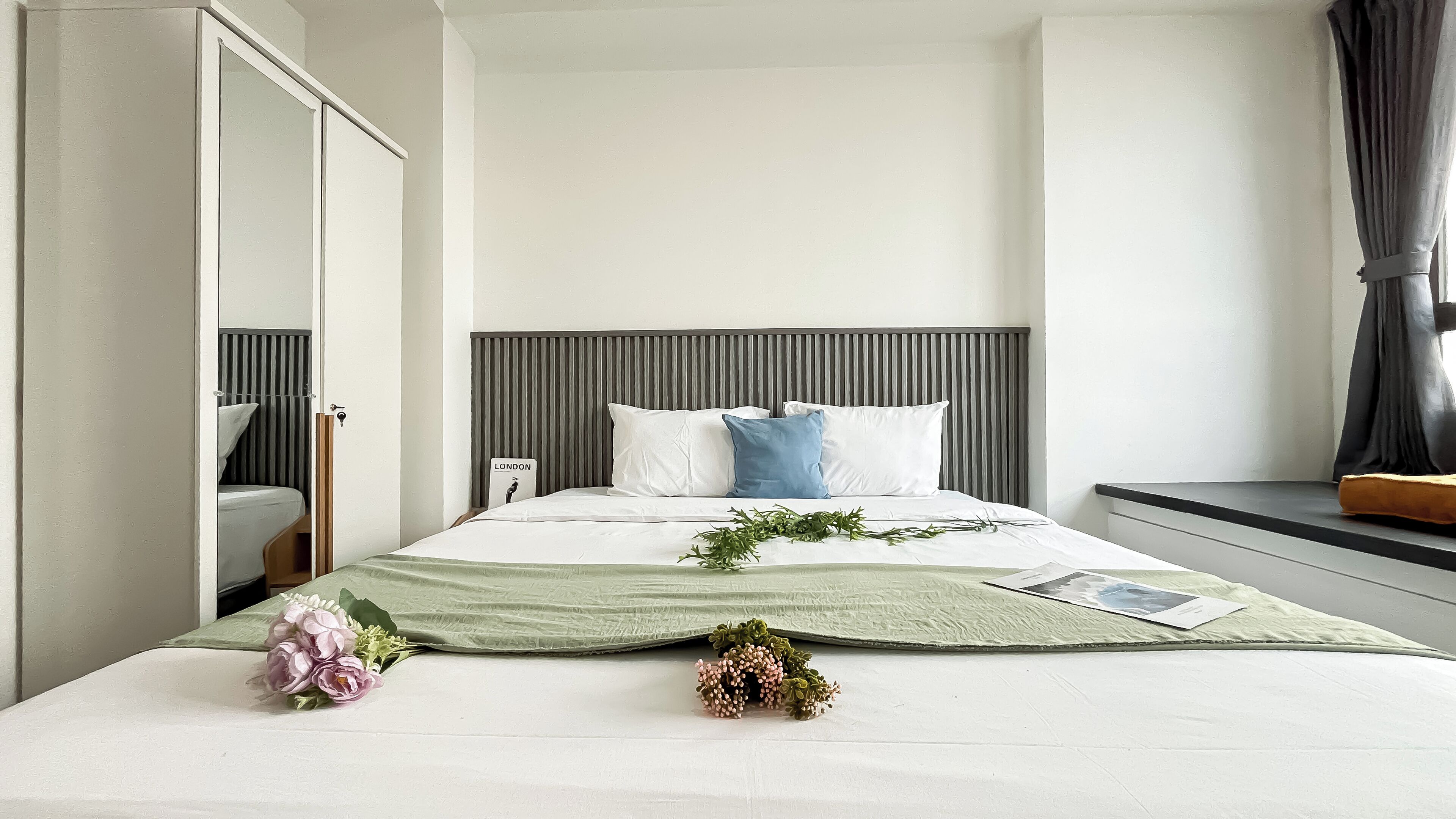 Un lit bien fait, avec une couvre-lit verte, des oreillers blancs et une composition florale décorative.