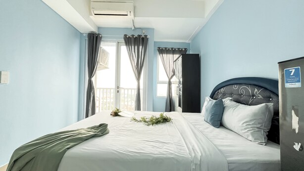 A bedroom with a bed, a window with curtains, a ceiling fan, and a sign indicating a 7-year compressor warranty. - Studio Apartment Poris 88 Near Batu Ceper Station (Tangerang)