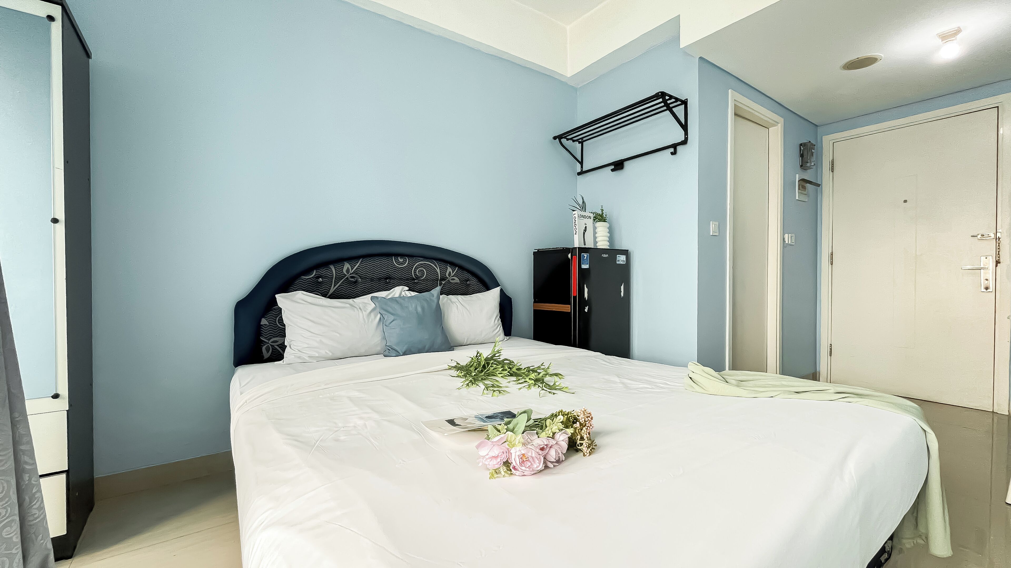 Una cama bien hecha con un edredón blanco, un cabecero negro y un ramo de flores sobre la cama.