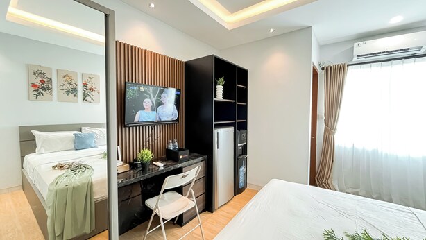 A modern hotel room with a bed, a desk with a computer, a TV, and a wardrobe.