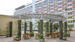 A covered outdoor seating area with stone pillars and potted plants, surrounded by a multi-story residential building.