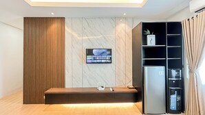 Una habitación de hotel moderna con un mostrador de recepción de madera, un televisor de pantalla plana montado en una pared de mármol, un minibar negro y un amplio ventanal con cortinas.