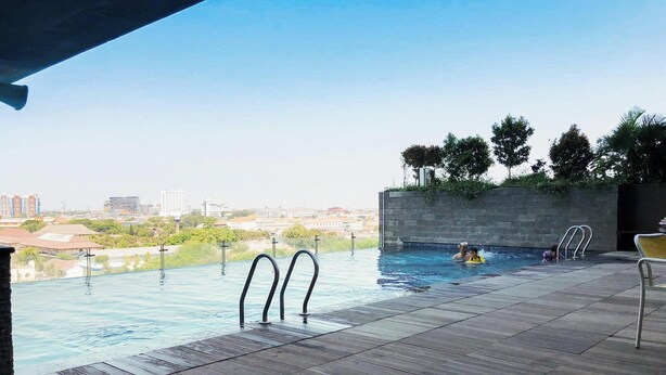 Ein Pool ohne Ende mit Blick auf die Stadtlandschaft, eine Holzterrasse und eine Steinmauer mit Bäumen.