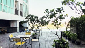 Eine Terrasse im Freien mit Tischen und Stühlen, umgeben von Topfpflanzen und Blick auf ein Gebäude.