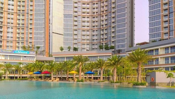 Un hotel moderno con un amplio área de piscina, palmeras y un letrero que dice 'Outdoors'.