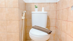 A white toilet with a towel on top, a small potted plant, and a toilet paper holder. - Simple Style 2Br At Green Pramuka City Apartment (Jakarta)