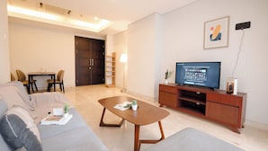 A modern living room with a sofa, a coffee table, a TV on a wooden stand, and a dining area with chairs and a table. - Strategic Place 2Br Apartment With Private Lift Masterpiece The Epicentrum Kuningan (Jakarta)