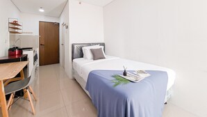 Un dormitorio con cama, escritorio y silla, una pequeña cocina y una puerta.