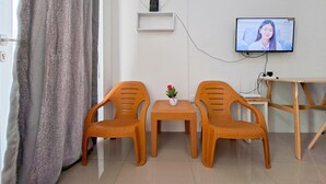 Una habitación con dos sillones de mimbre, una mesita con planta en maceta, un televisor fijado a la pared y un escritorio de madera.