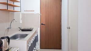 Una cocina compacta con un lavamanos, una tetera y una puerta de madera.