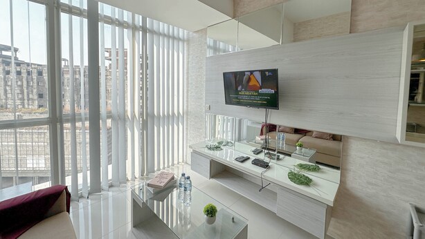 Ein modernes Wohnzimmer mit großem Fenster, einem wandmontierten Flachbildfernseher, einem Glastisch und einem schlichten Konsolentisch mit Dekoration.
