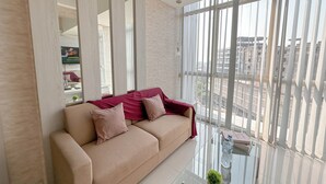 Ein modernes Wohnzimmer mit einem beigefarbenen Sofa, einem Glastisch und einem großen Fenster mit Blick auf die Stadt.