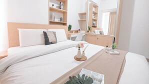 A neatly arranged hotel room with a large bed, a bedside table with a vase of flowers, a mirror, and built-in shelving with books and decorative items.