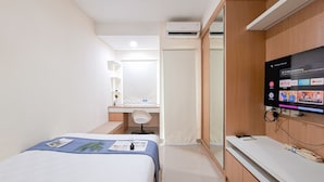 A hotel room with a bed, a desk, a TV mounted on the wall, and an air conditioning unit. - Urban Minimalist Studio Apartment At B Residence (Pagedangan)