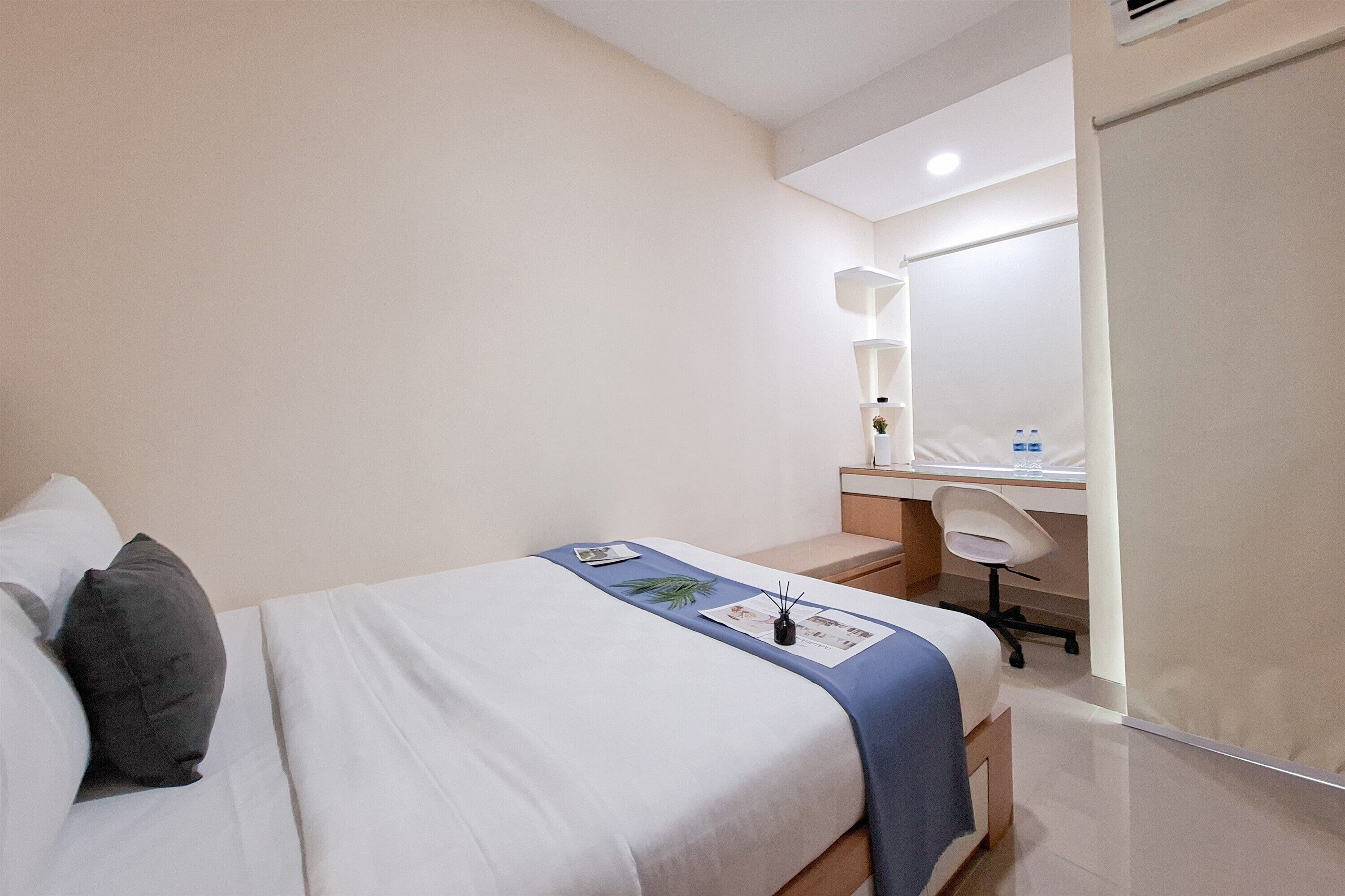 A hotel room with a bed, a desk, a chair, and a mirror.