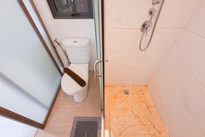 Un baño con inodoro, ducha y un escalón pequeño que da acceso a la zona de la ducha.