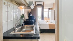 A compact kitchen with a sink, stove, and cabinets, leading to a bedroom with a bed and a window.