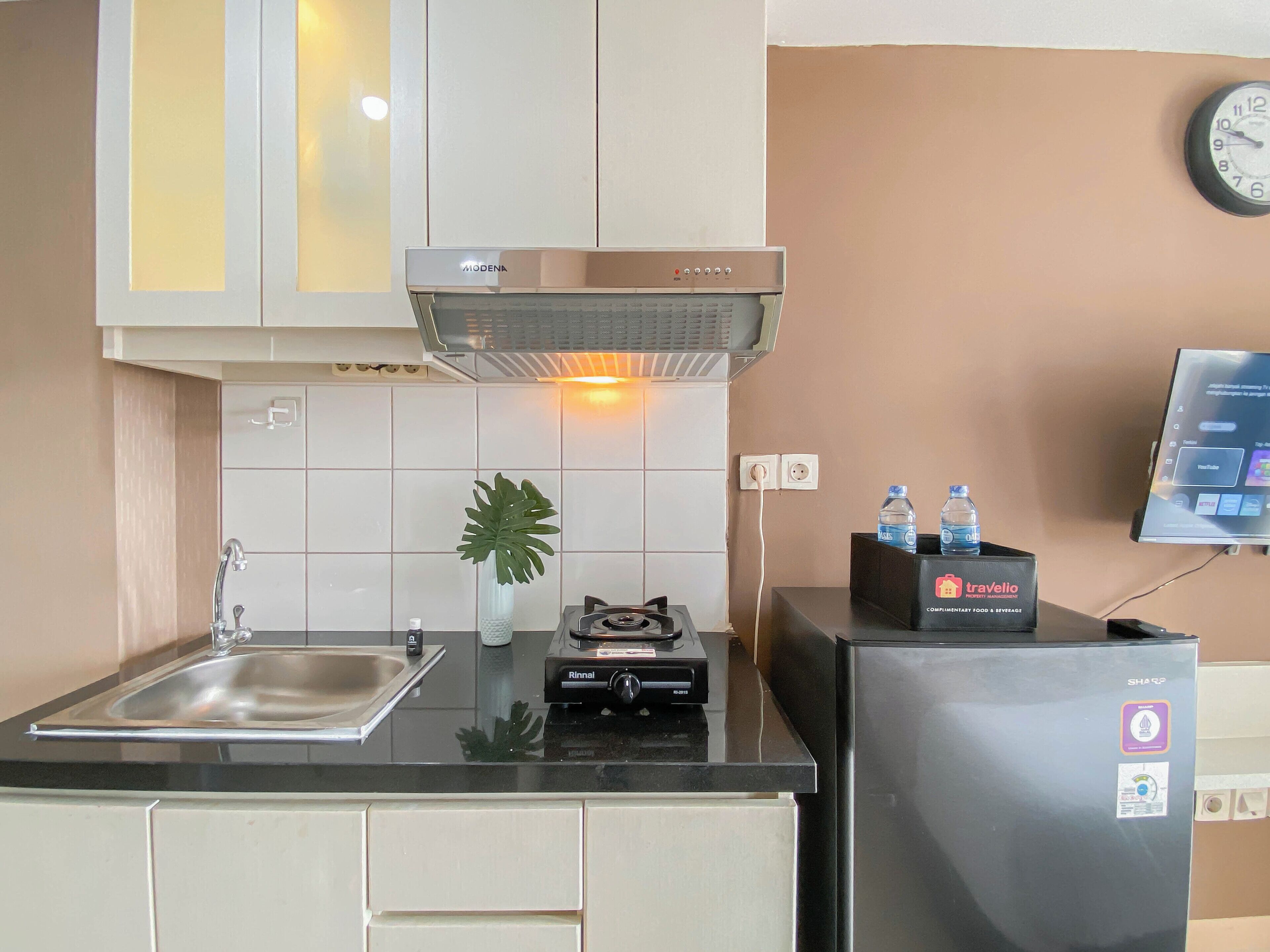 Una cocina con lavaplatos, estufa y refrigerador, una planta y un reloj en la pared.