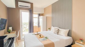 A hotel room with a bed, a desk with a computer, an air conditioner, and a view of the city.
