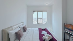 A hotel room with a bed, a window with a city view, and a television on a stand. - Simple Style Studio At The City Square Surabaya Apartment (Surabaya)