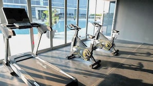 A gym with treadmills and stationary bikes, large windows, and a modern interior. - Simple Style Studio At The City Square Surabaya Apartment (Surabaya)