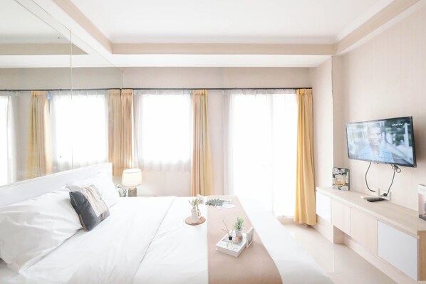 A hotel room with a large bed, a TV, a bedside table, and a window with curtains. - Strategic Studio Apartment Signature Park Grande Near Ciliwung Lrt Station (Jakarta)