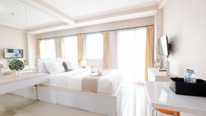 A hotel room with a bed, bedside table, TV, and a desk with a chair. - Strategic Studio Apartment Signature Park Grande Near Ciliwung Lrt Station (Jakarta)