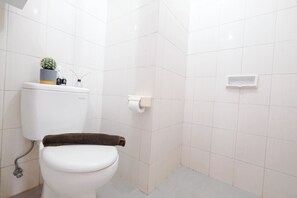 A bathroom with a toilet, a small shelf with a plant, and a toilet paper holder. - Strategic Studio Apartment Signature Park Grande Near Ciliwung Lrt Station (Jakarta)