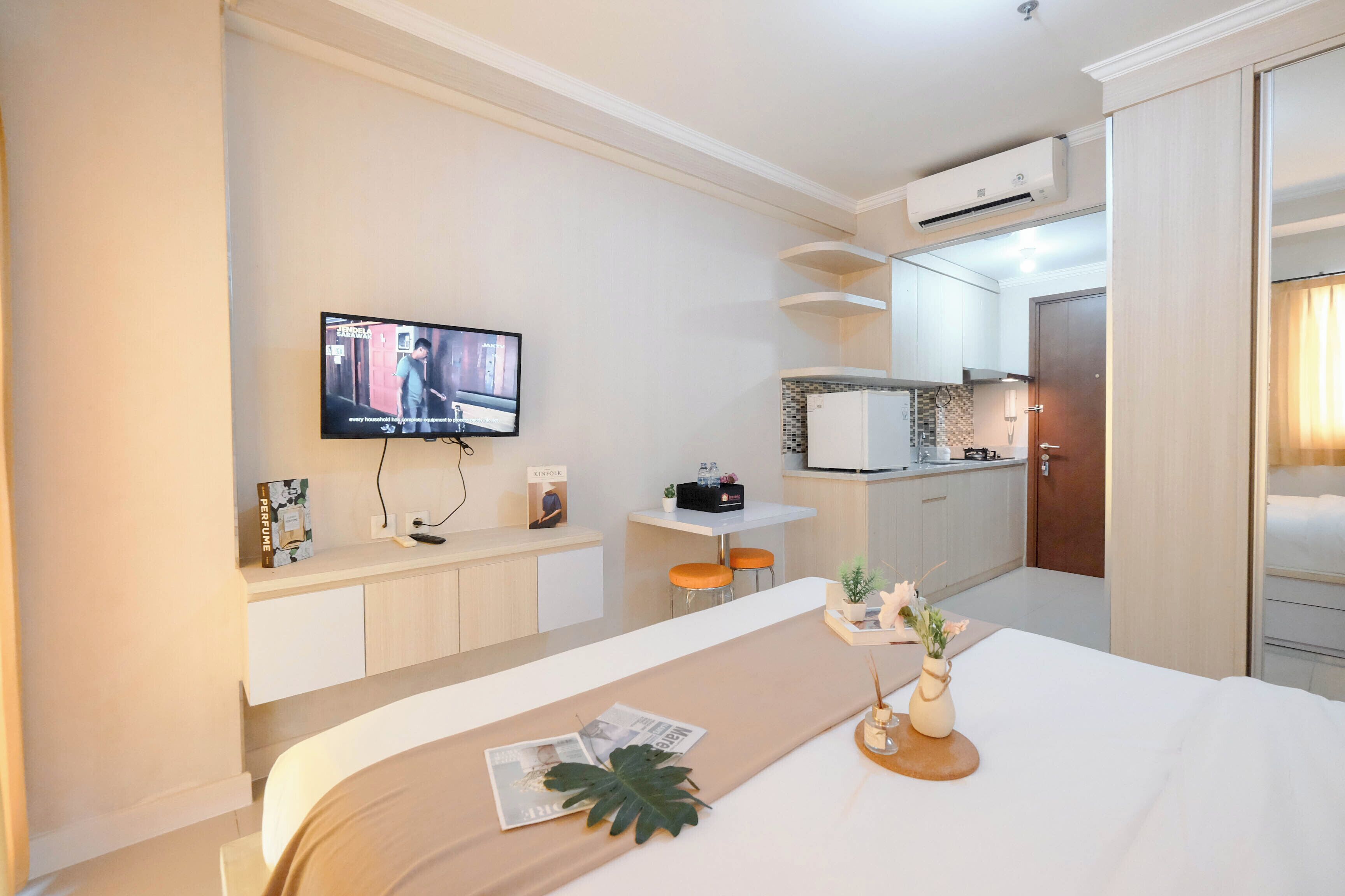 A hotel room with a bed, a TV mounted on the wall, a kitchenette, and a bathroom.