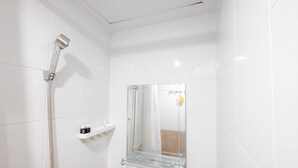 A bathroom with white tiles, a glass shelf, a shower, and a mirror. - Neutral Tone 2Br At Green Pramuka City Apartment (Jakarta)