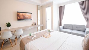 A modern hotel room with a bed, a TV mounted on the wall, a sofa, and a desk with chairs. - Modern Studio Near Taman Ismail Marzuki At Apartment Menteng Park (Jakarta)