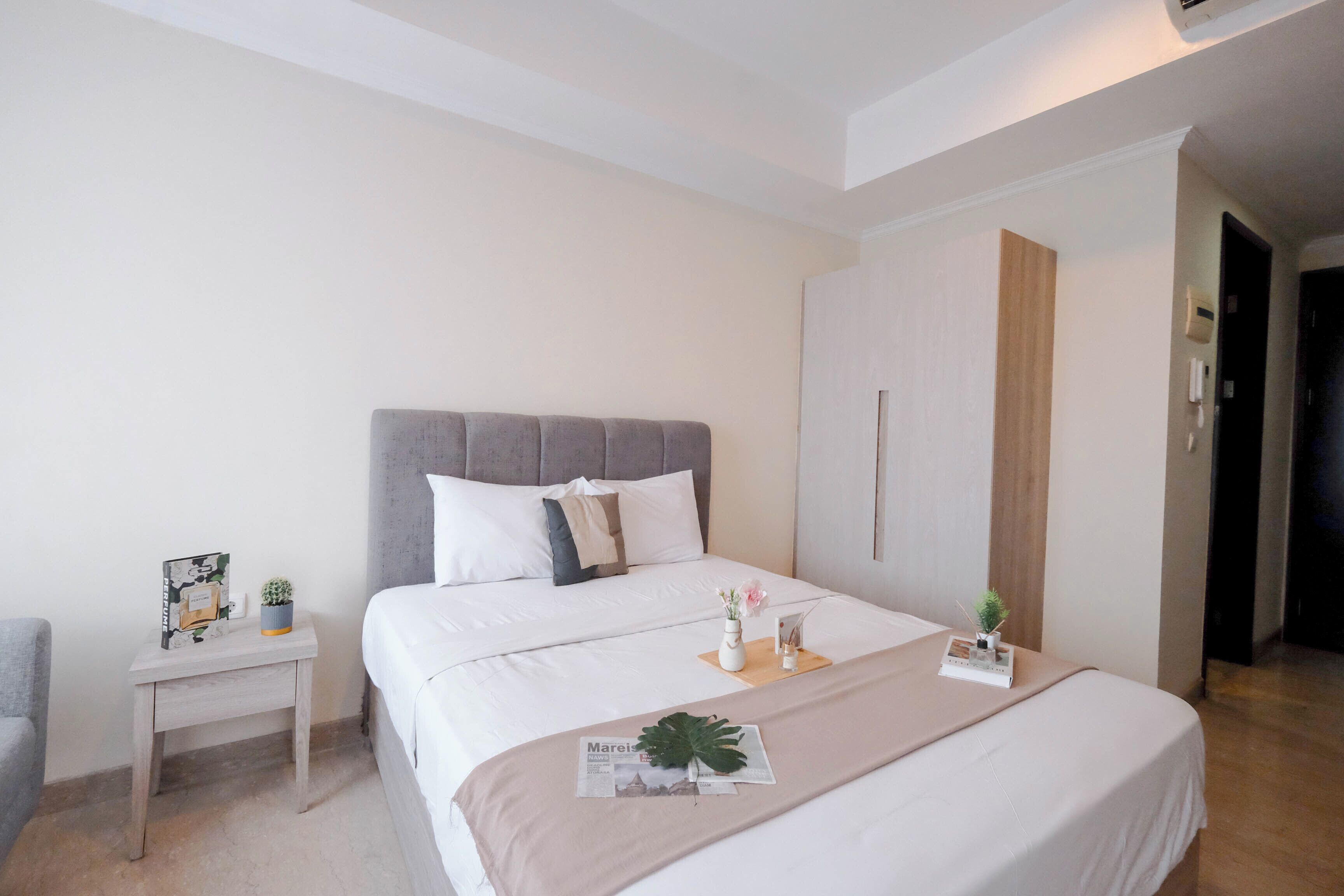 A neatly arranged hotel room with a large bed, a bedside table, a small chair, and a door leading to another room.