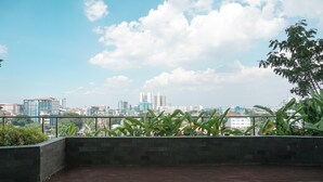 A rooftop terrace with a city skyline view, featuring a mix of modern and traditional buildings, and a metal railing with greenery in the foreground. - Modern Studio Near Taman Ismail Marzuki At Apartment Menteng Park (Jakarta)