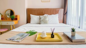 A neatly arranged hotel room with a bed, bedside table, and a window with curtains. - Soft Pastel Minimalist 3Br At Pollux Chadstone Apartment (Cikarang)