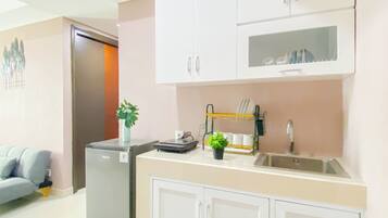 A modern kitchen with white cabinets, a built-in dishwasher, a sink, and a small countertop with a plant and a dish rack.