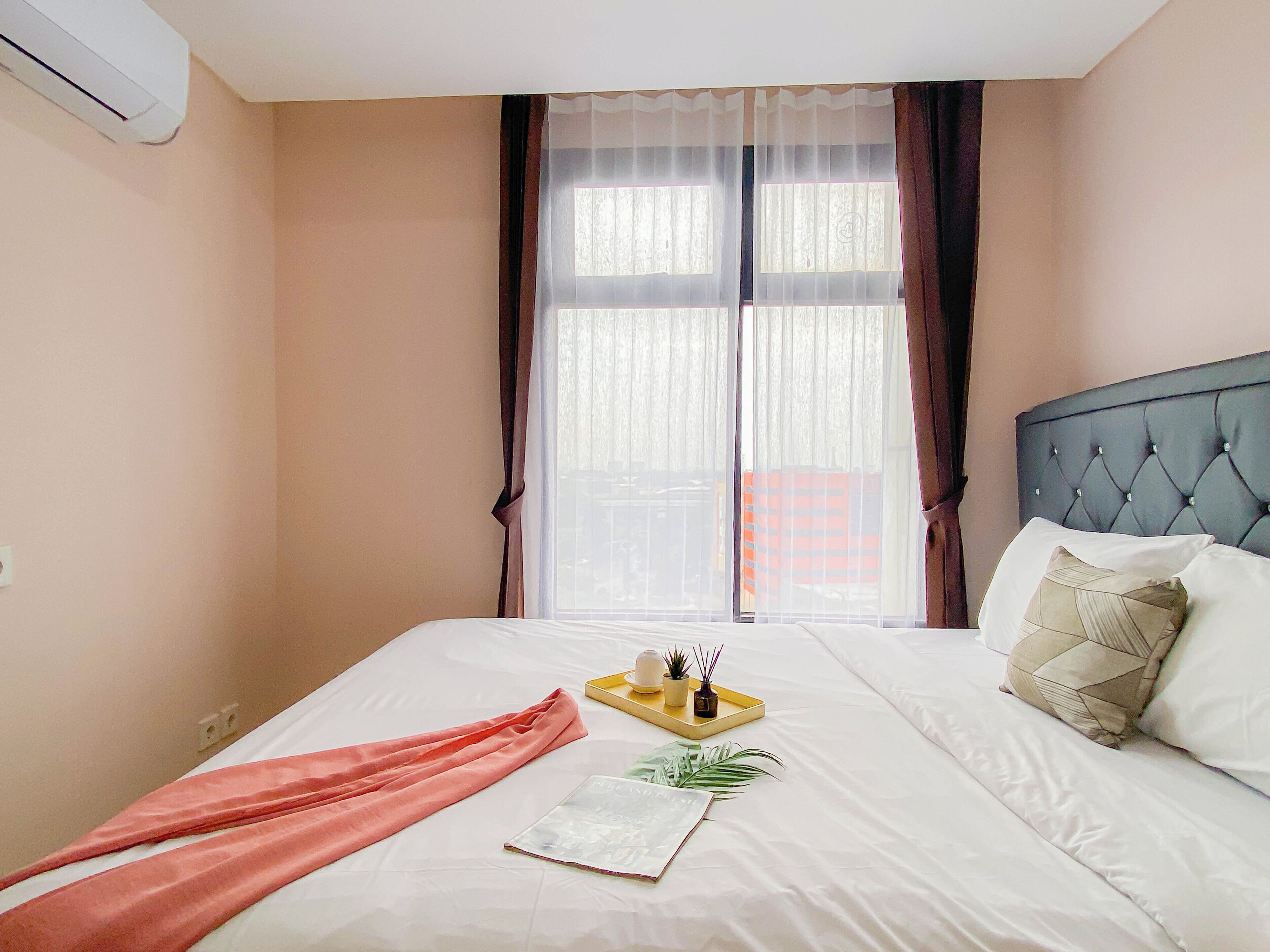 A neatly made bed with white linens, a pink towel, and a tray with a plant and a candle.