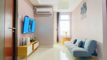 A living room with a flat-screen TV, a sofa, a small table with a vase, and an air conditioning unit on the wall.