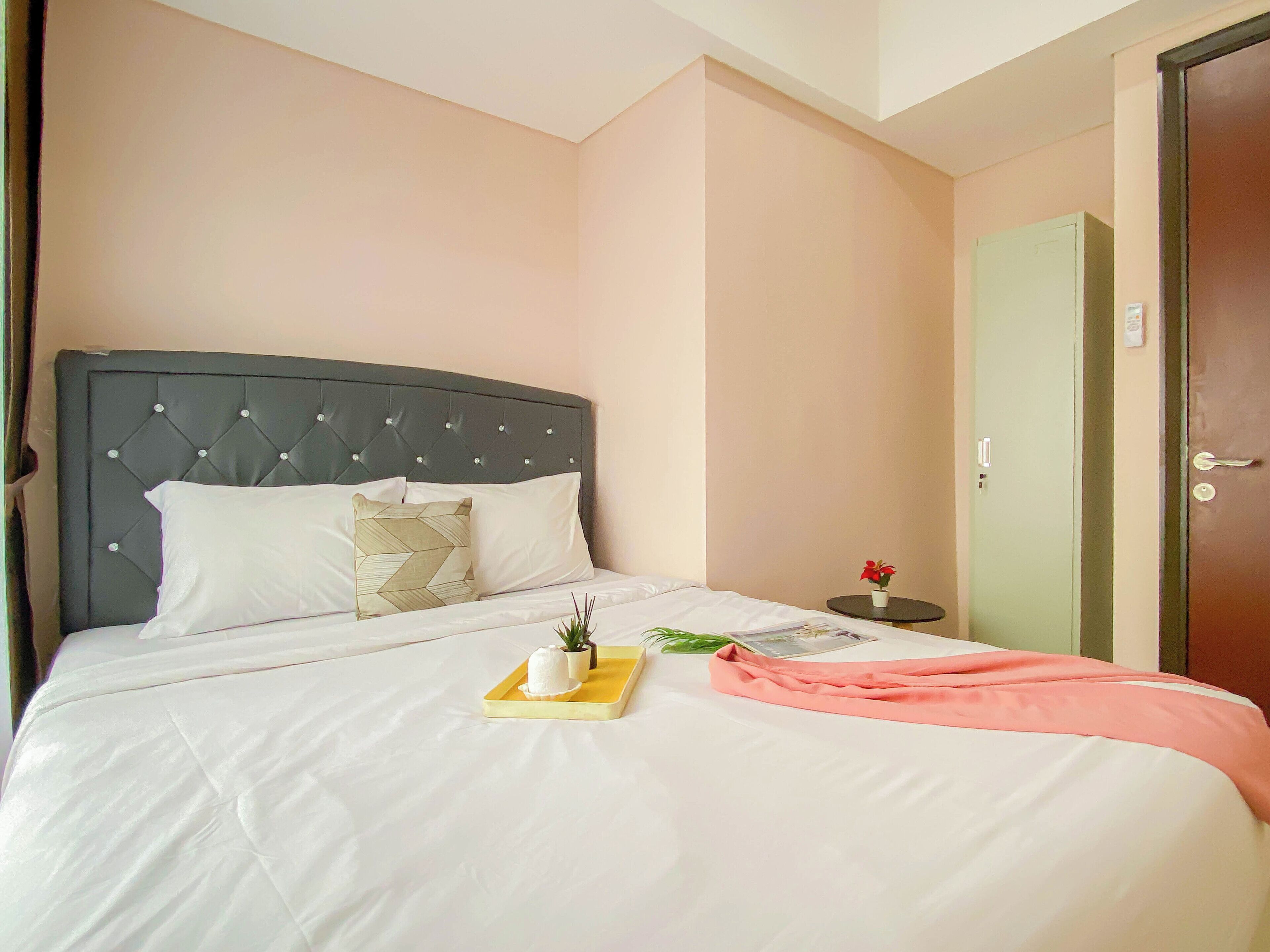 A neatly made bed with a grey headboard, white bedding, and a small bedside table with a red flower vase.