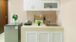 A compact kitchen with white cabinets, a sink, and a small refrigerator. - Soft Pastel Minimalist 3Br At Pollux Chadstone Apartment (Cikarang)