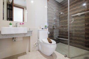 A modern bathroom with a white toilet, a sink, and a glass shower enclosure. - Boho Touch 2Br Apartment With Extra Room At Lucky Tower Residence (Jakarta)