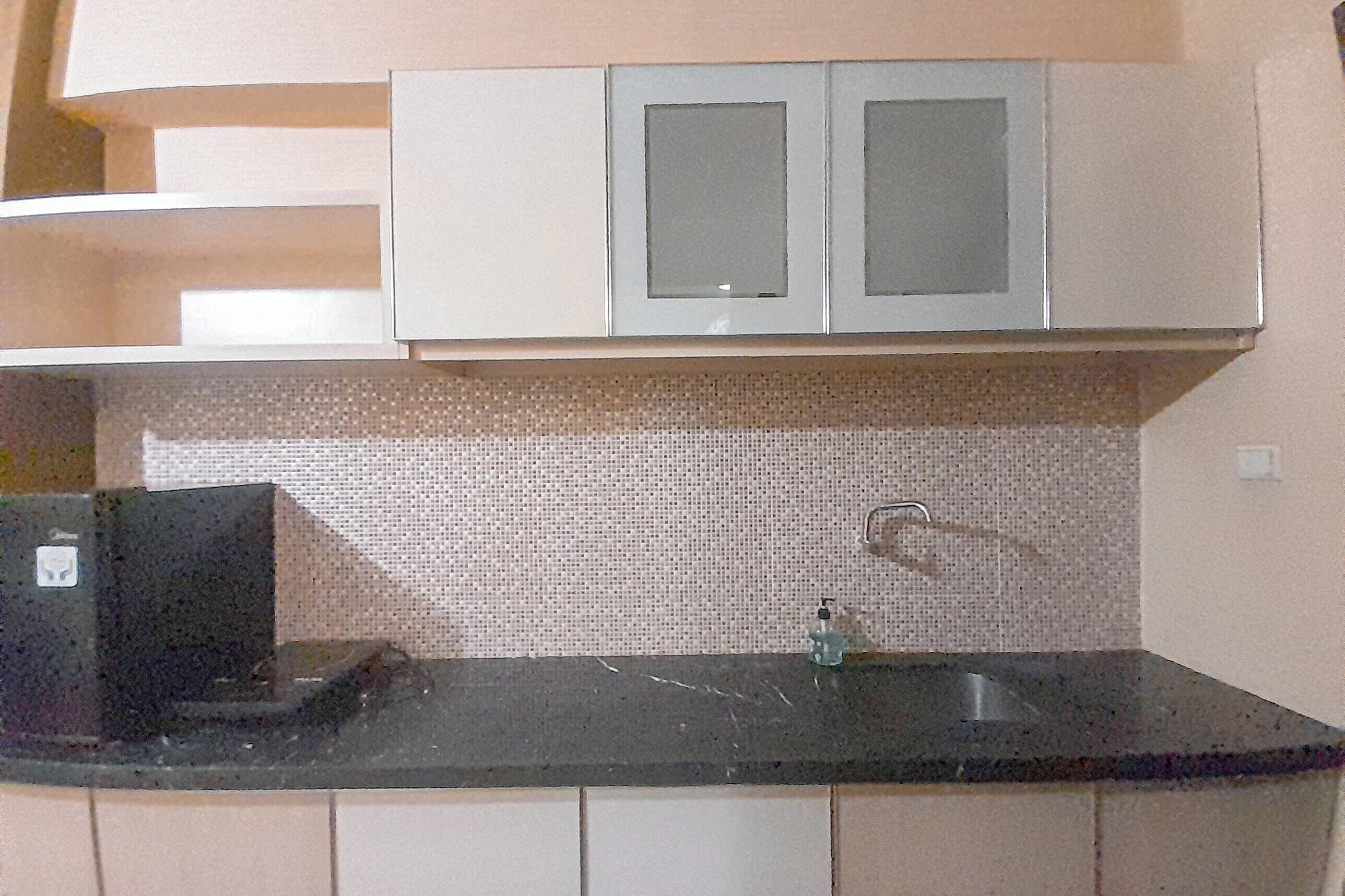 A kitchen with a black countertop, a sink, and white cabinets with glass doors.