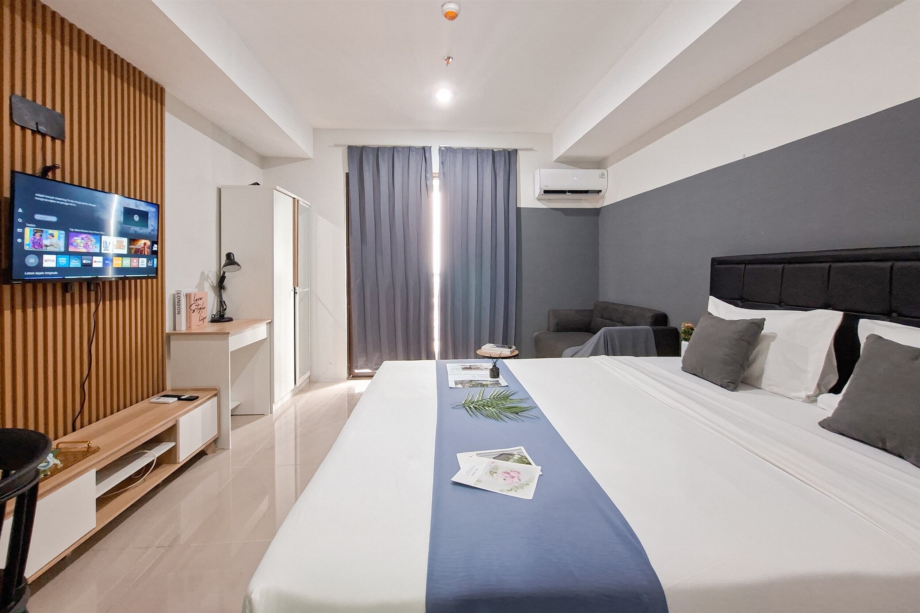 Een moderne hotelkamer met een groot bed, een flatscreen televisie aan de muur, een bureau met een stoel en een raam met gordijnen.