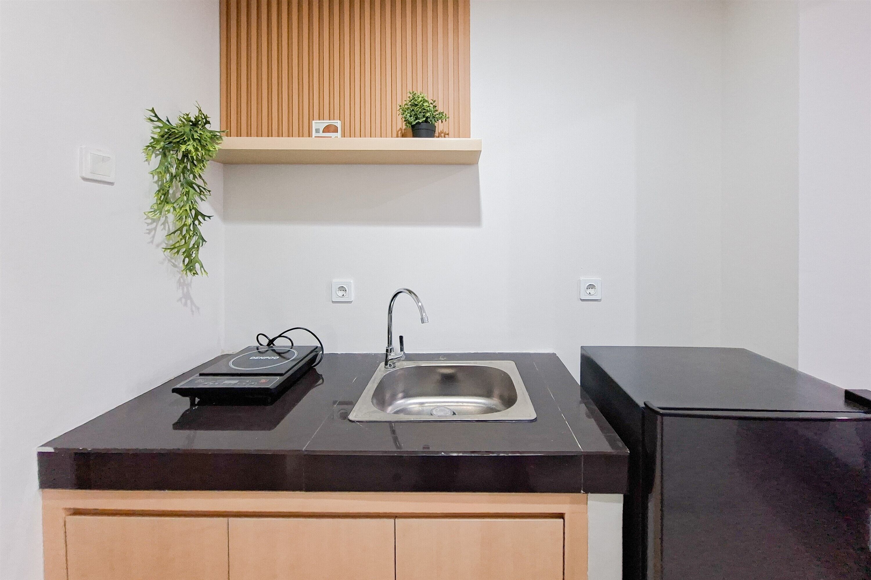 A kitchen with a black countertop, stainless steel sink, wooden cabinets, a black refrigerator, a wooden shelf with two potted plants, and a wall-mounted plant.