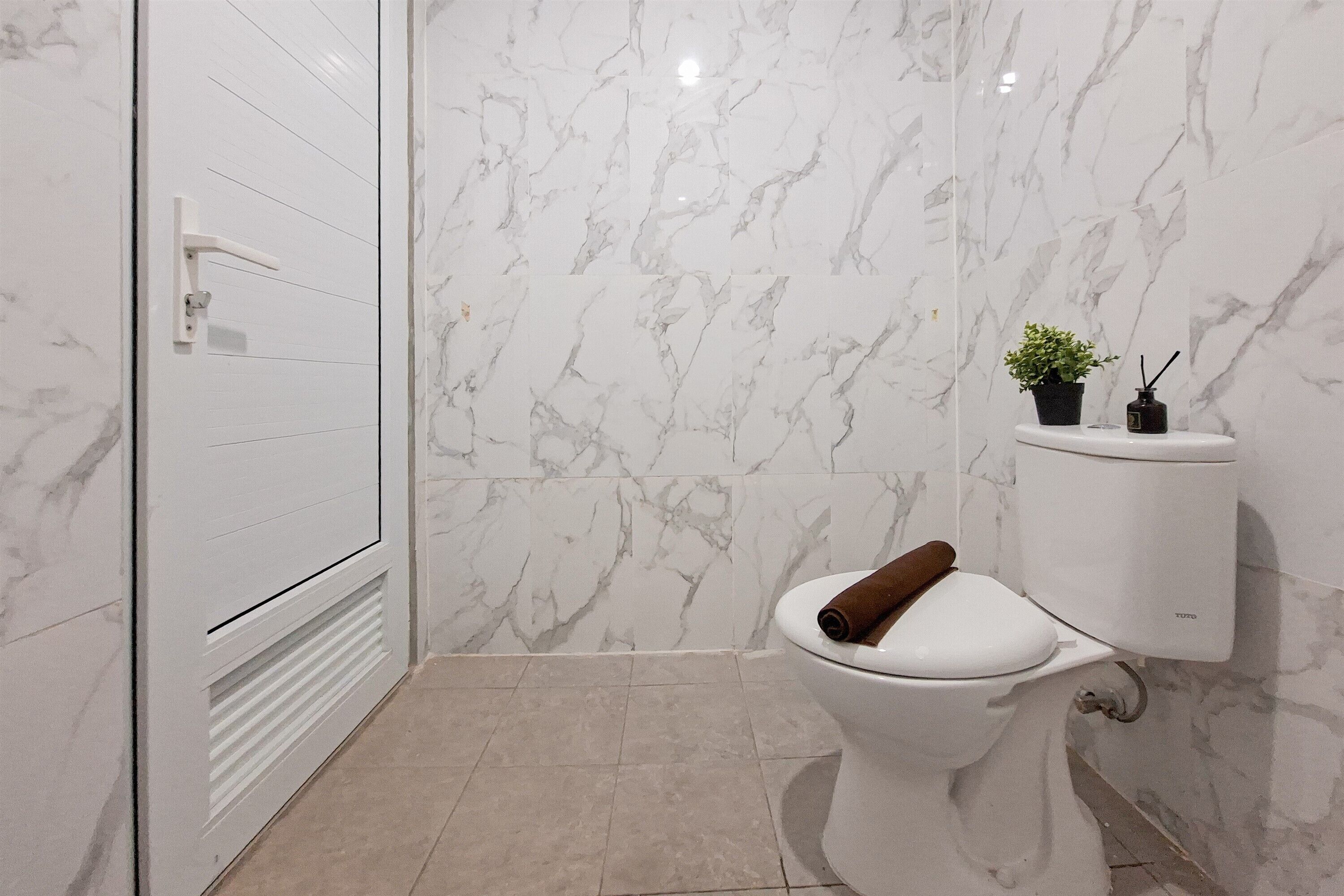 Une salle de bain comprenant des toilettes, un espace douche et un mur en marbre.