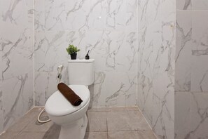 Un baño con inodoro, una pequeña planta en maceta y un escobillón de pared.