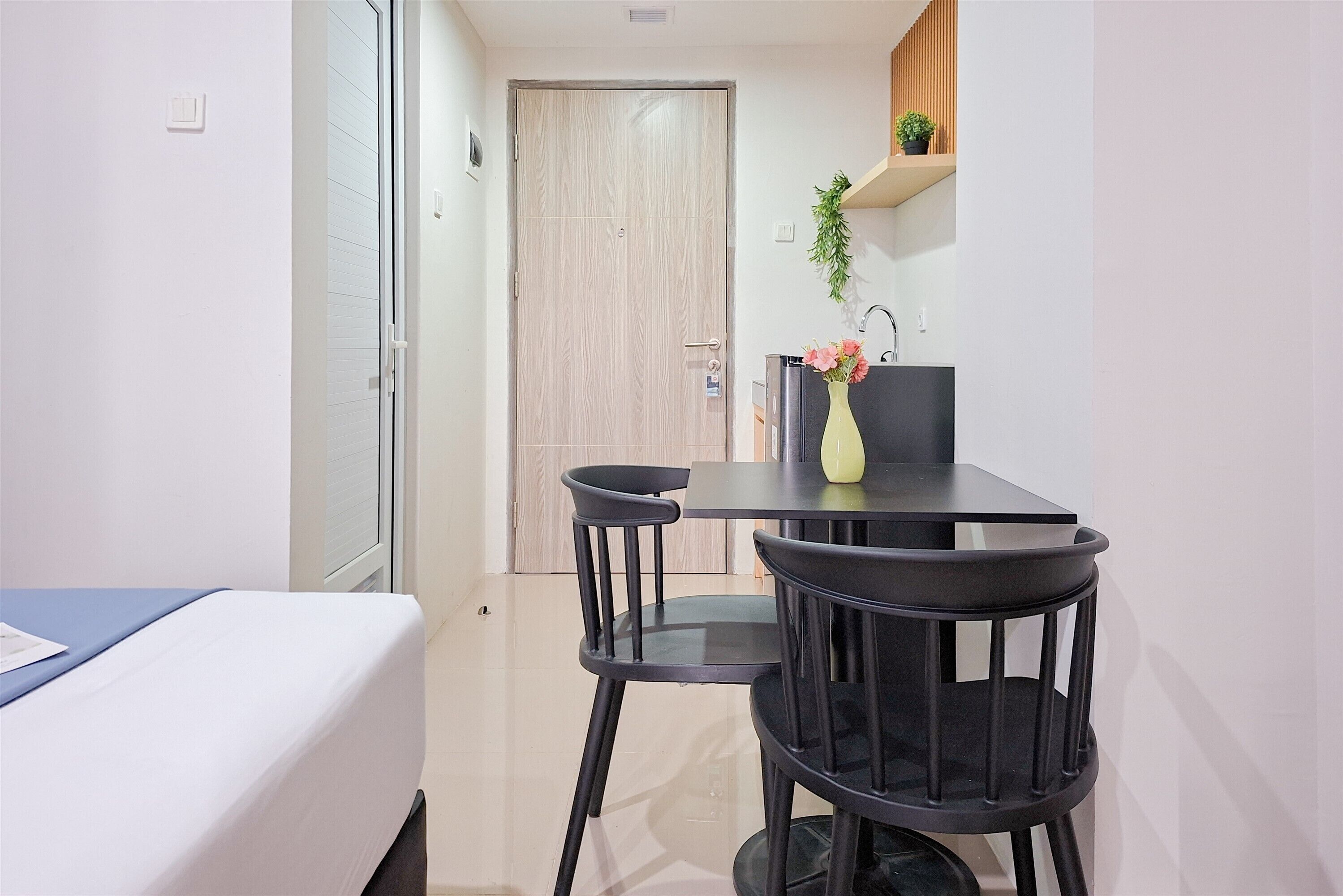 Una habitación pequeña con cama, una mesa y dos sillas, un lavamanos y una puerta de madera.