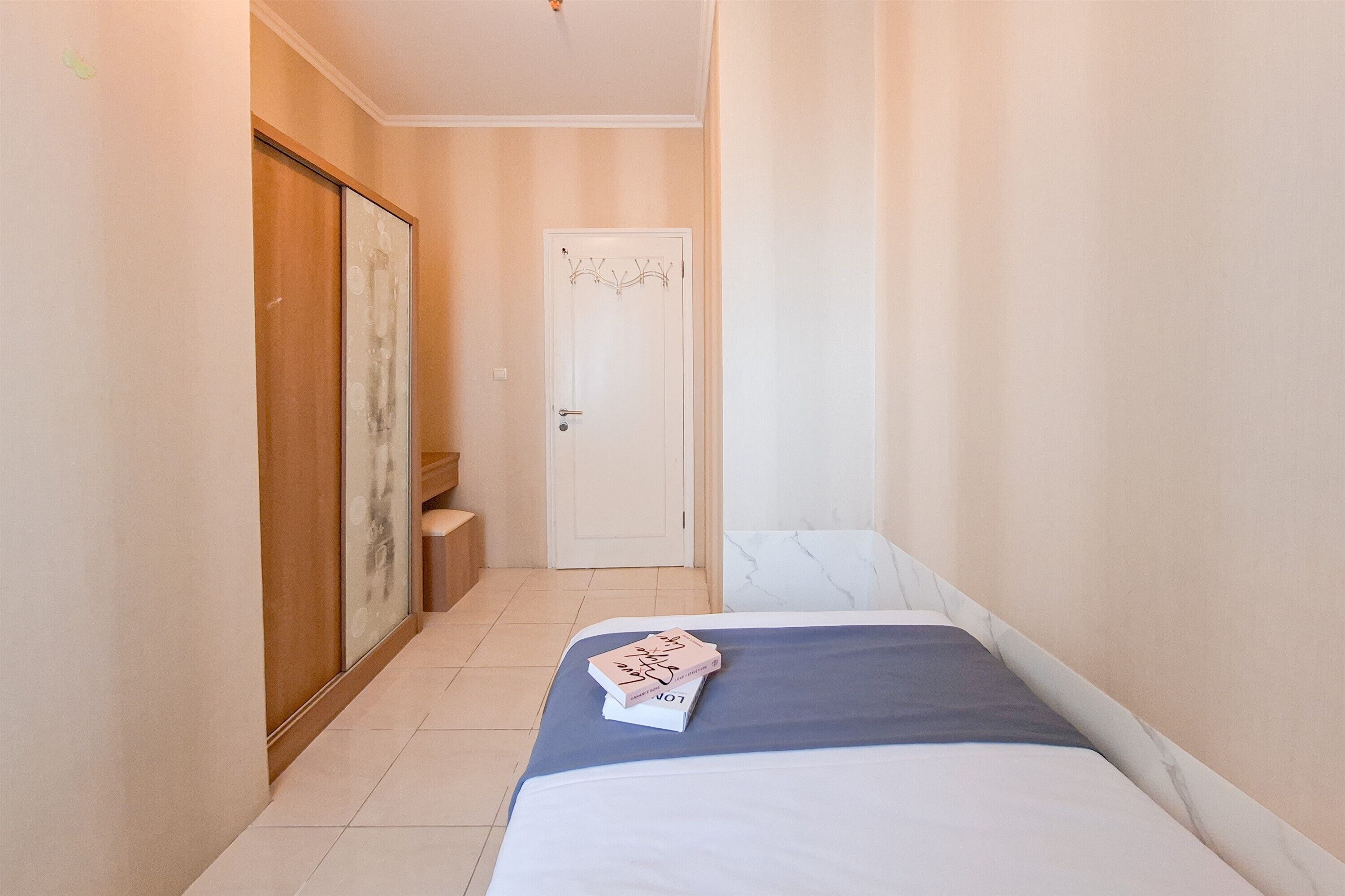 A narrow hallway leading to a door with a decorative design, a bed with a blue bedspread, and a small bedside table.