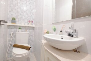 A bathroom with a toilet, a sink, and a shower. There are plants and a towel on the toilet. - Wooden Accent Studio At Tokyo Riverside Pik 2 Apartment (Teluknaga)